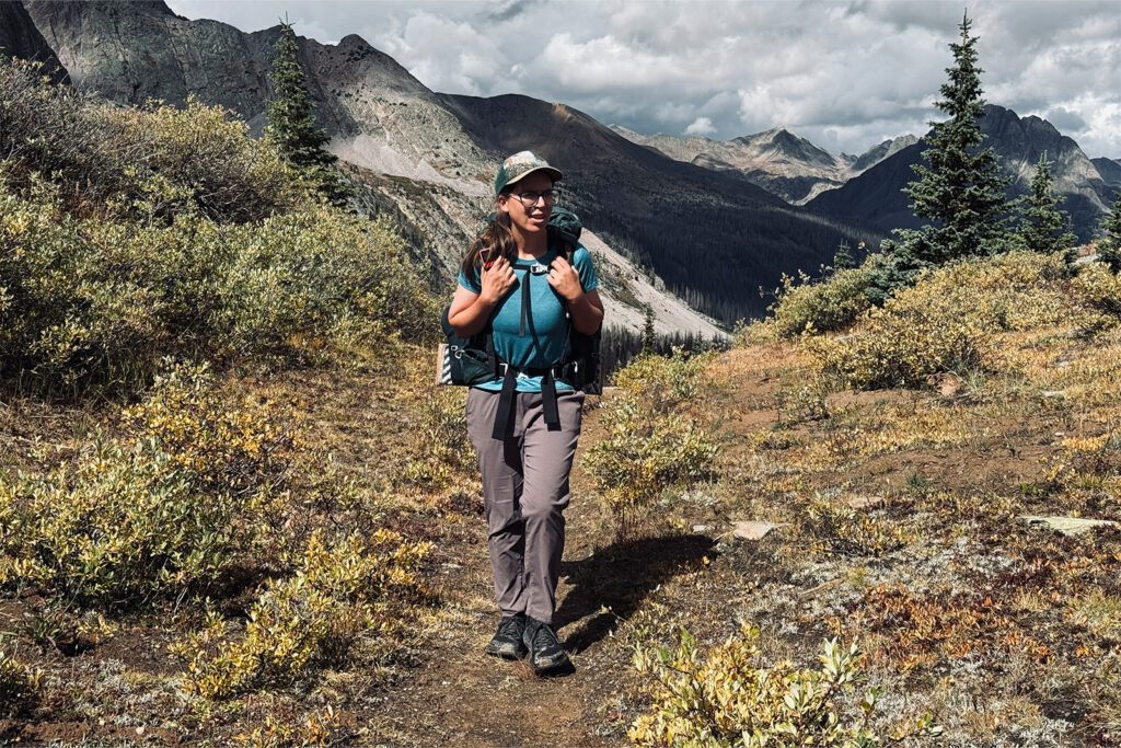 A person wearing a backpack walking on a mountain trail, illustrating budget backpacking gear in use.