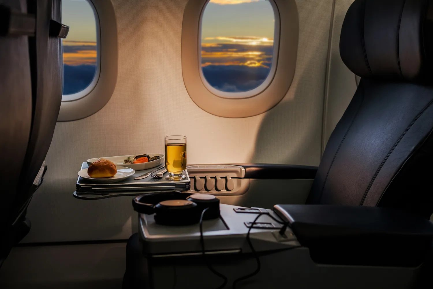 Airplane seat with meal tray on a table and sunset visible through the window.
