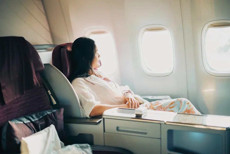 A passenger seated in business class is looking out the airplane window.