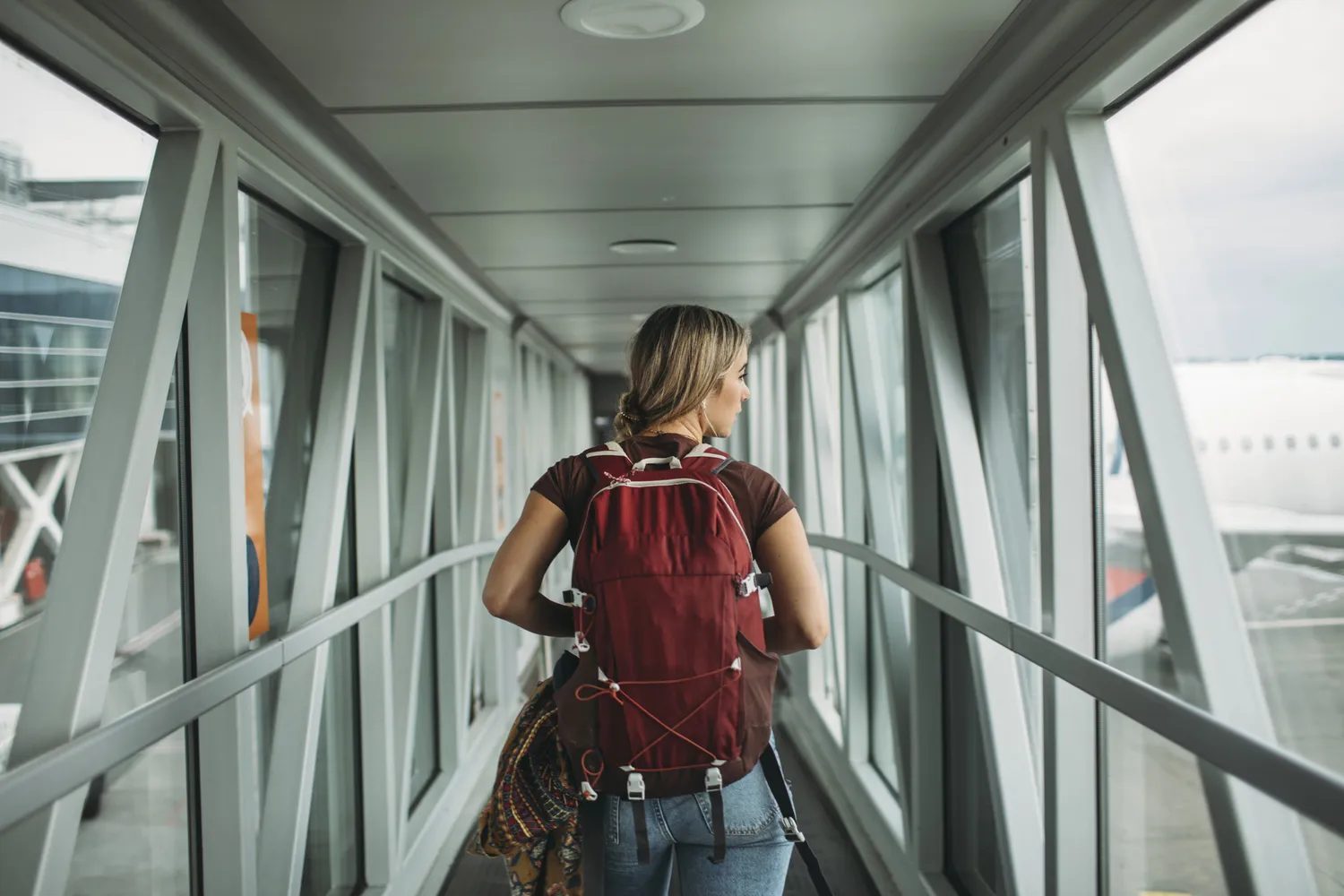 Person with a backpack walking through an airport jet bridge towards a plane