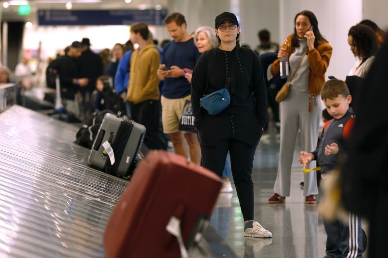 Passengers waiting at baggage claim, facing potential extra travel costs.