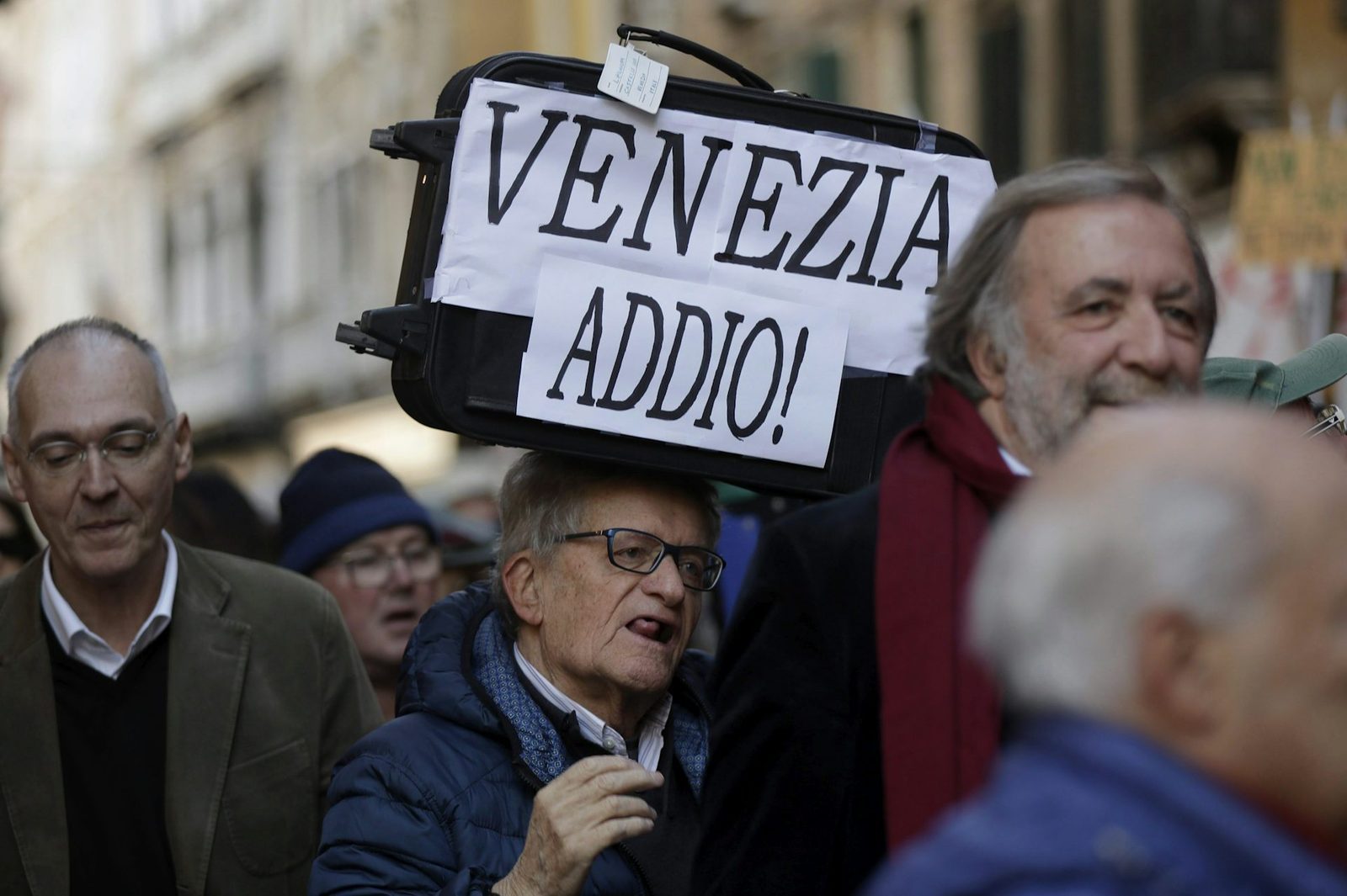 A protester in Venice holds a sign reading 'Venezia Addio', expressing frustration with overtourism.
