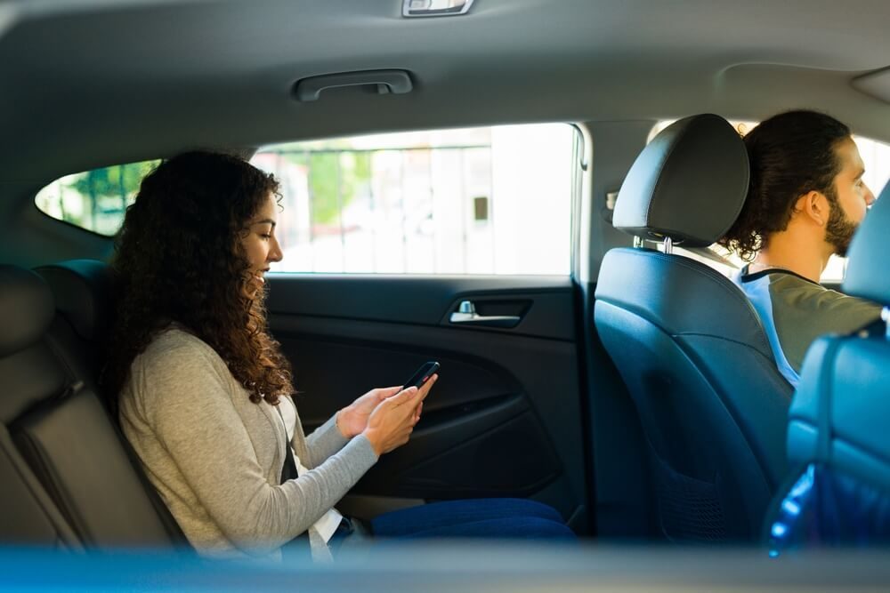 Happy woman passenger using the mobile app of a ride share service on her smartphone - cheap rideshare insurance.