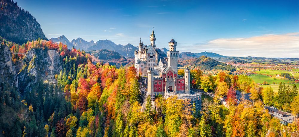 A picturesque aerial view of Neuschwanstein Castle surrounded by vibrant autumn foliage and mountains in the background.