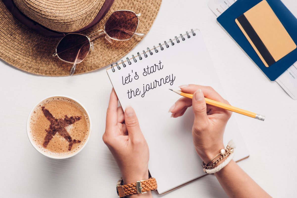Traveler planning a trip budget with notebook, coffee, passport and ticket on a table