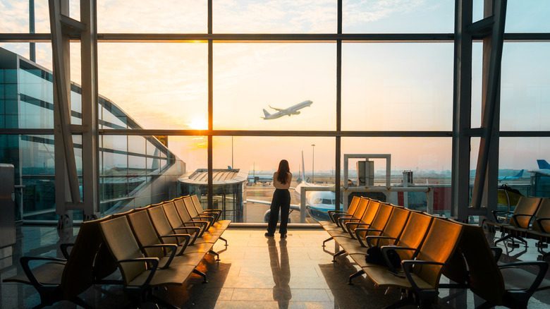 Backview of a female at an empty airport watching a plane take off