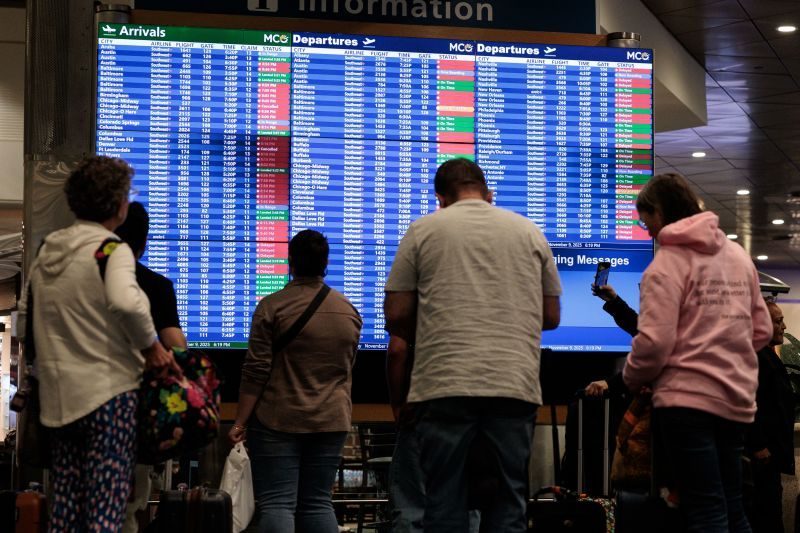 Passengers look at flight delays on a departure board at Orlando International Airport.