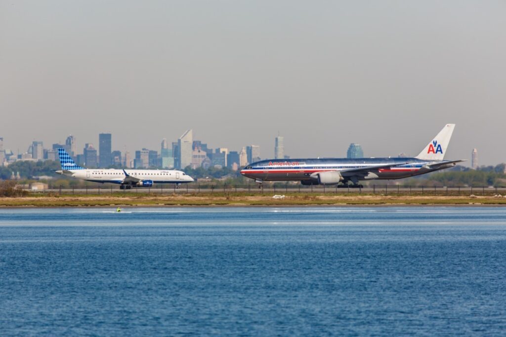 jet blue and american airlines planes standing on a runway next to a river