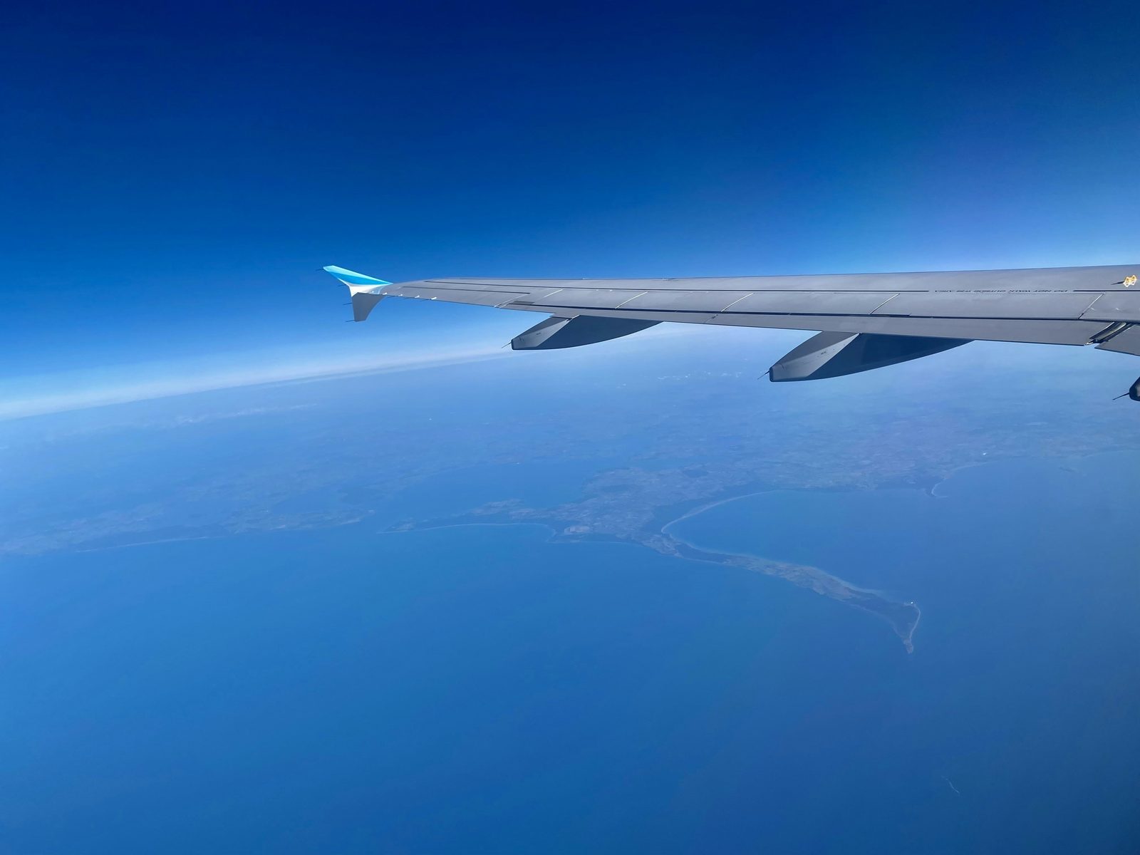 Airplane flying over the ocean near a long bridge, symbolizing long journeys with multiple flight segments