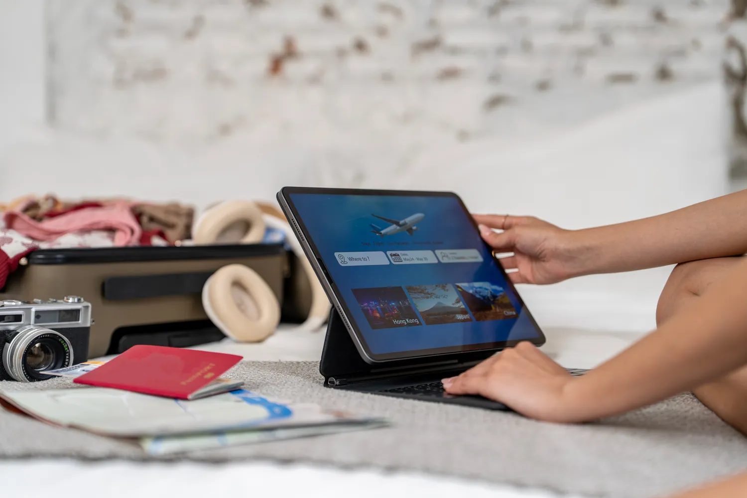 Person using a tablet travel items and an open suitcase nearby