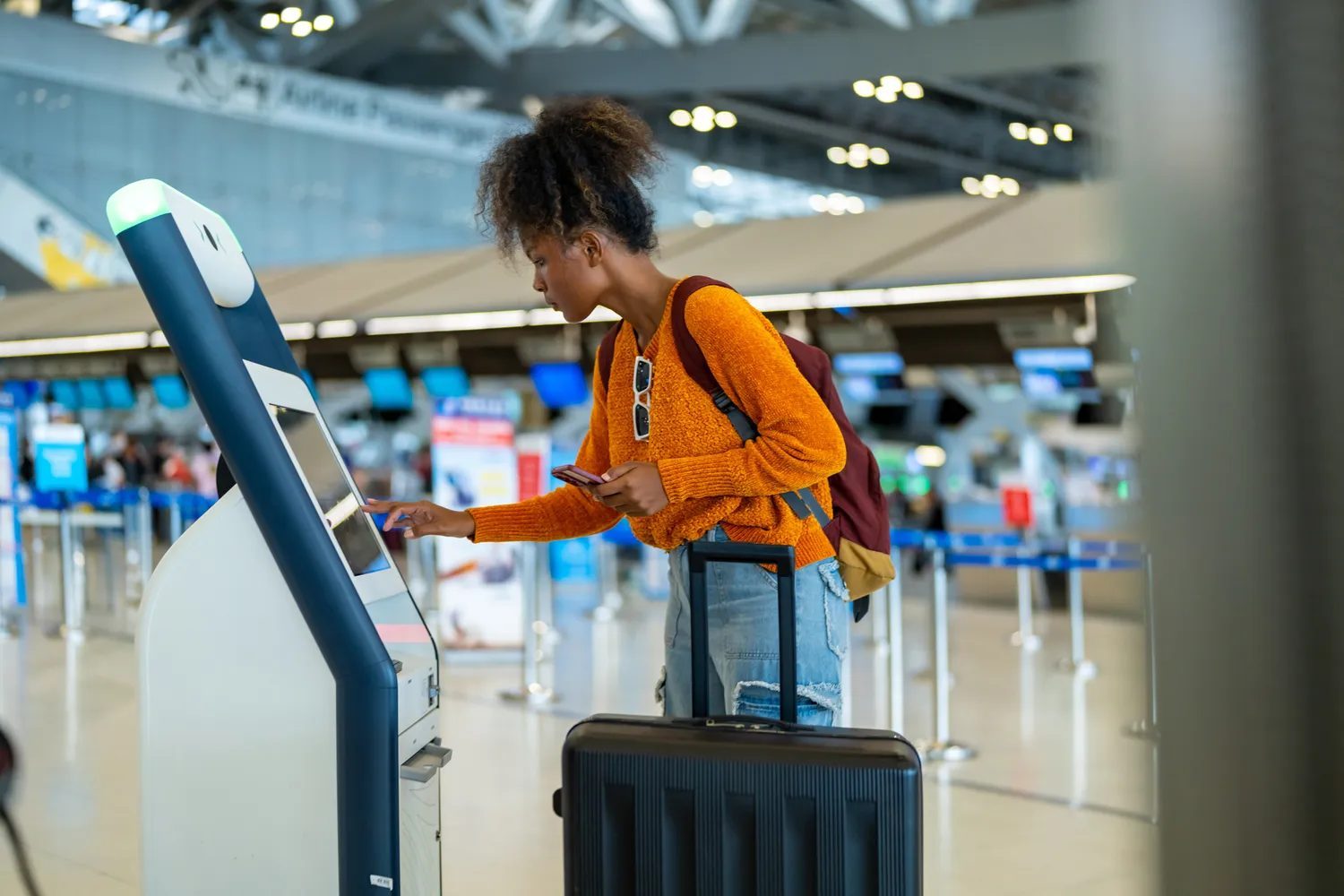 Traveler using a selfservice kiosk at an airport carrying a rolling suitcase